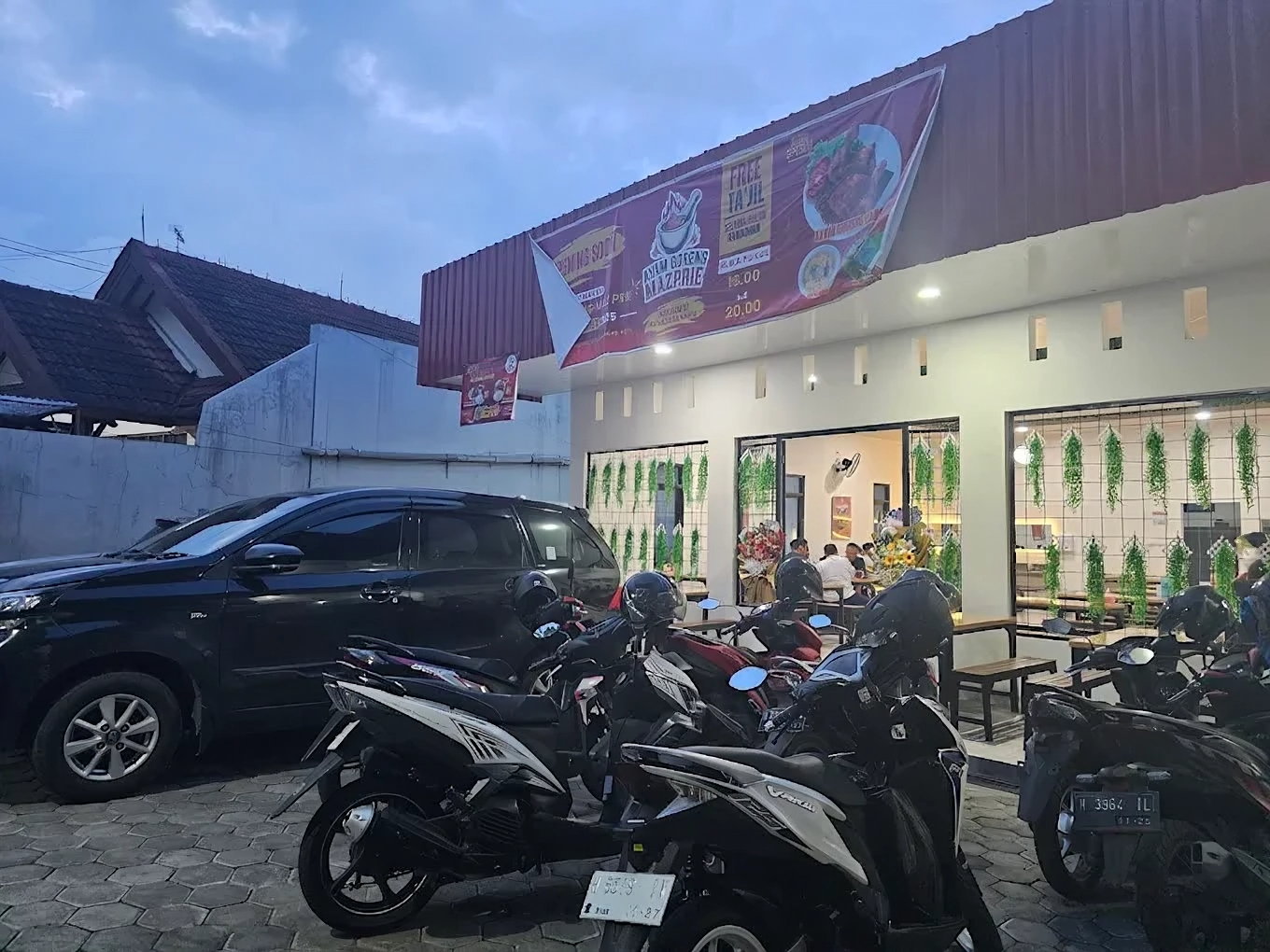Tampak depan Warung Ayam Goreng Laos Mazprie dengan area parkir kendaraan di malam hari Tampak depan Warung Ayam Goreng Laos Mazprie dengan area parkir kendaraan di malam hari